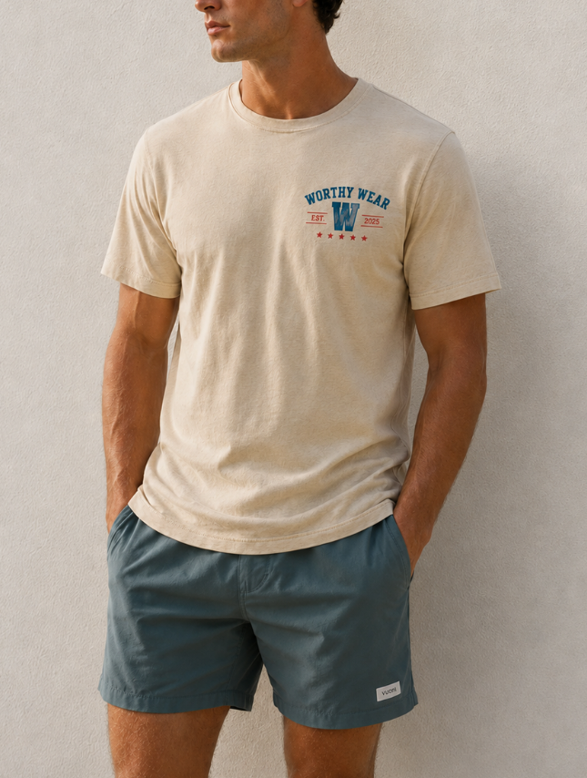 Beige vintage Goodness tee with "Worthy Wear" graphic, worn with teal shorts against a neutral background.