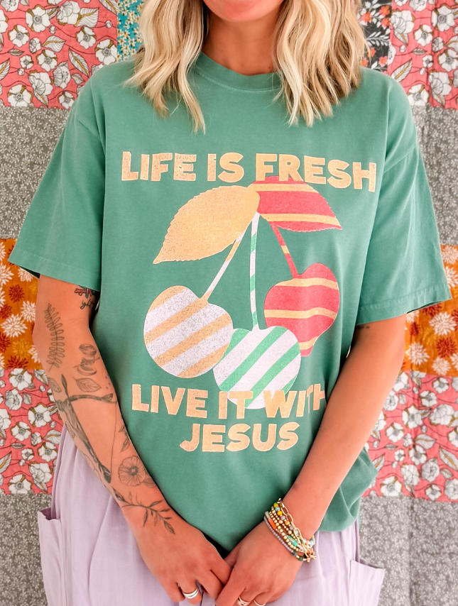 Life is Fresh tee in green featuring colorful cherry graphics and the text "Live it with Jesus" displayed prominently.