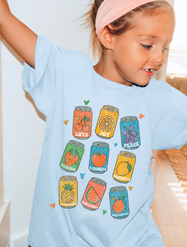Child wearing a light blue t-shirt with colorful graphic designs of cans and fruits.