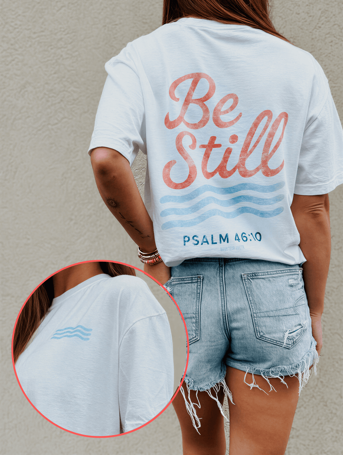 Be Still Tee in white with pink and blue text, worn with denim shorts, featuring a wave design and Psalm 46:10.