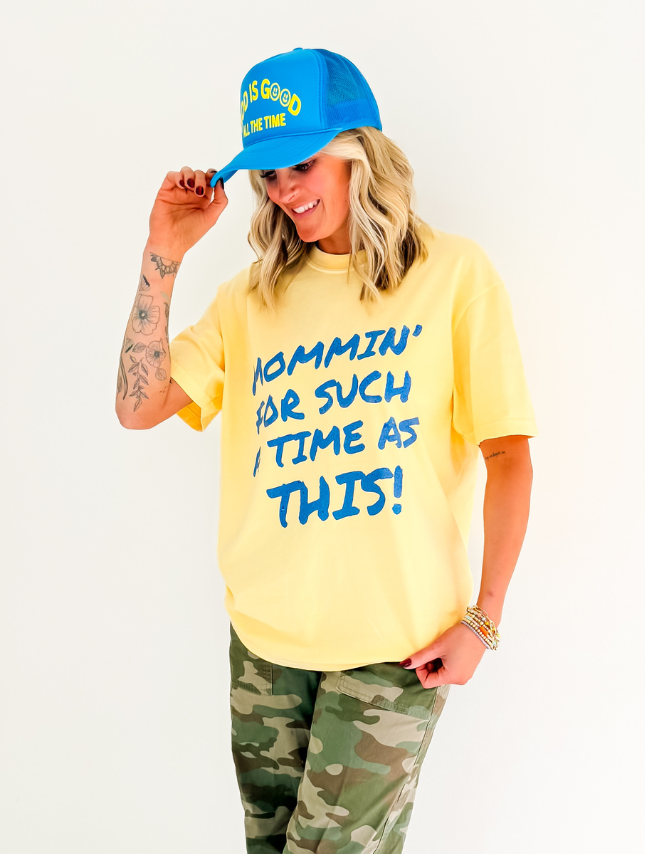 Yellow Mommin' Tee with blue text reading "Mommin' for such a time as this," paired with camo pants and a blue cap.