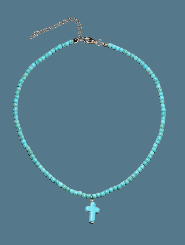 Turquoise beaded cross necklace with small beads and a central cross pendant on a blue background.